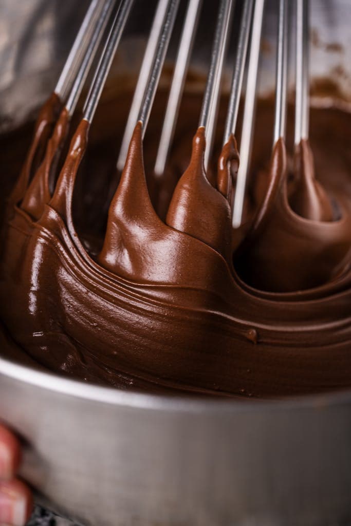 Sweet chocolate frosting being whipped in a metal bowl with an electric mixer for homemade desserts.
