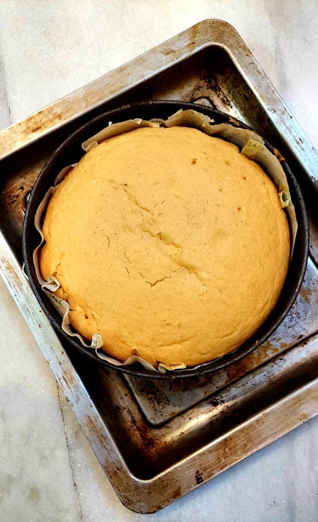 A delicious freshly baked cake resting in a round tin on a metal baking tray.
