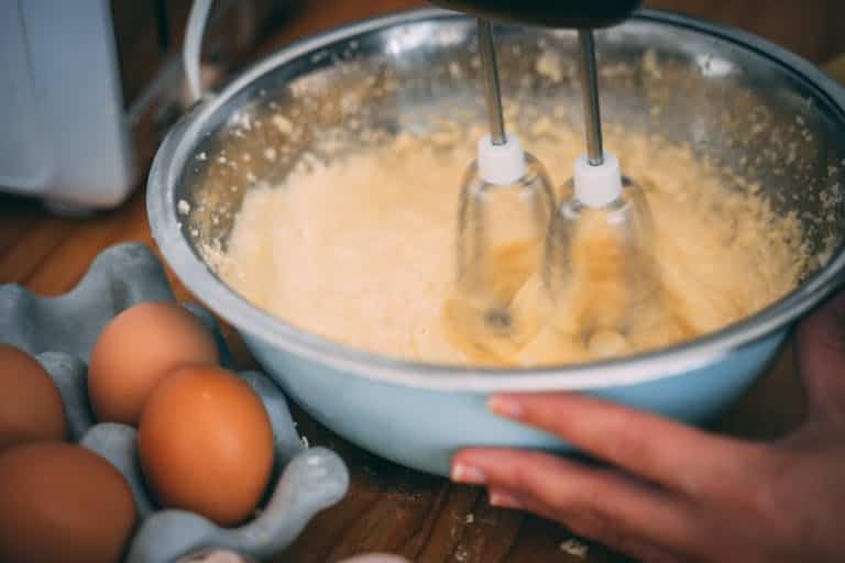 Close-up of batter being mixed in a bowl with eggs nearby on a wooden table.