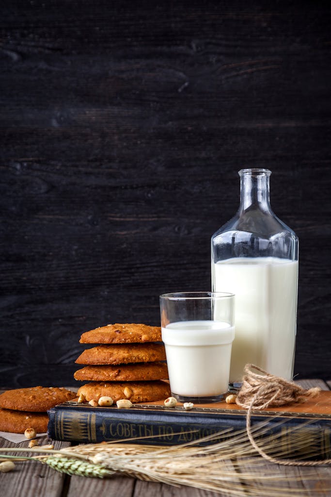Glass of buttermilk with stack of cookies, book, and bottle on a rustic wooden table.