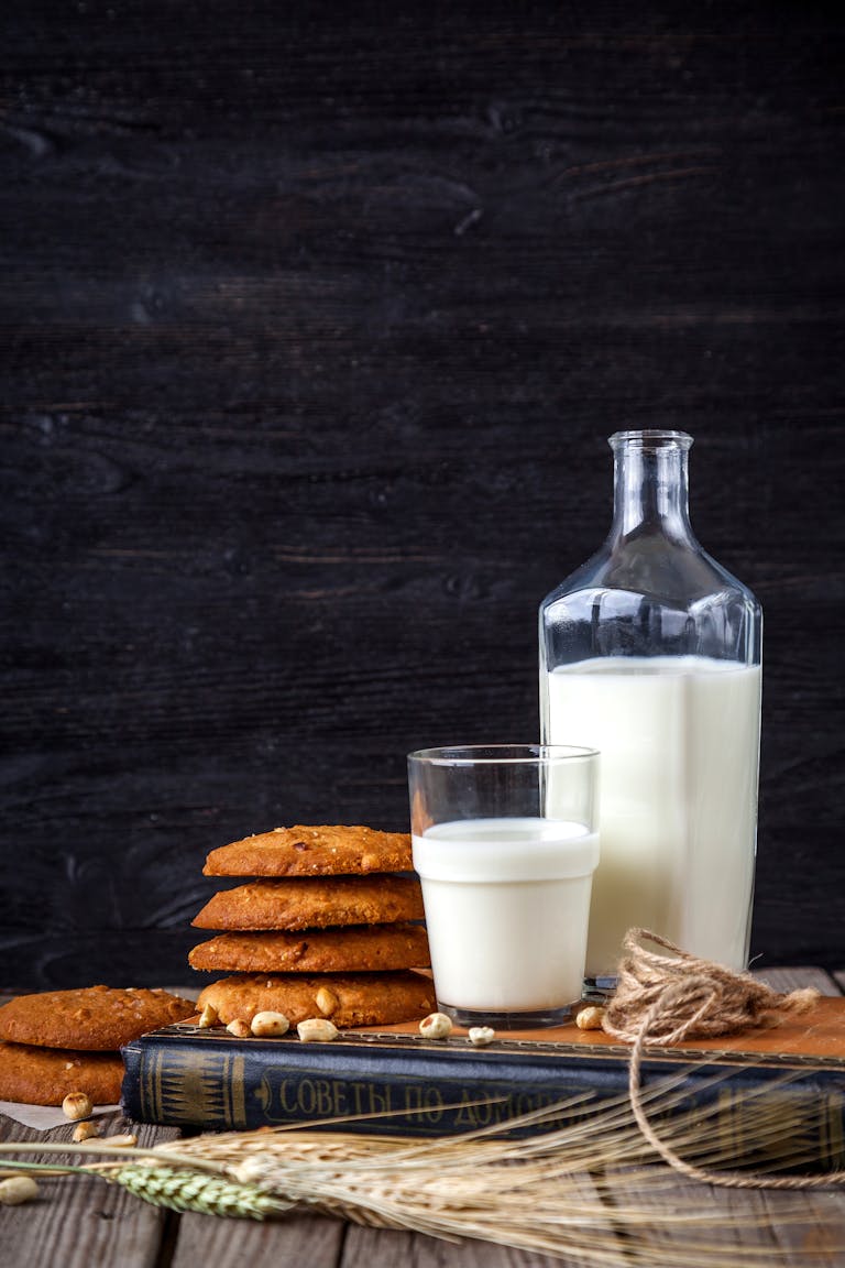Glass of buttermilk with stack of cookies, book, and bottle on a rustic wooden table.