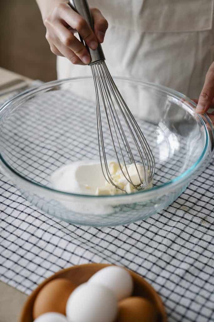 Person mixing ingredients in a glass bowl with a whisk, preparing dough or batter.