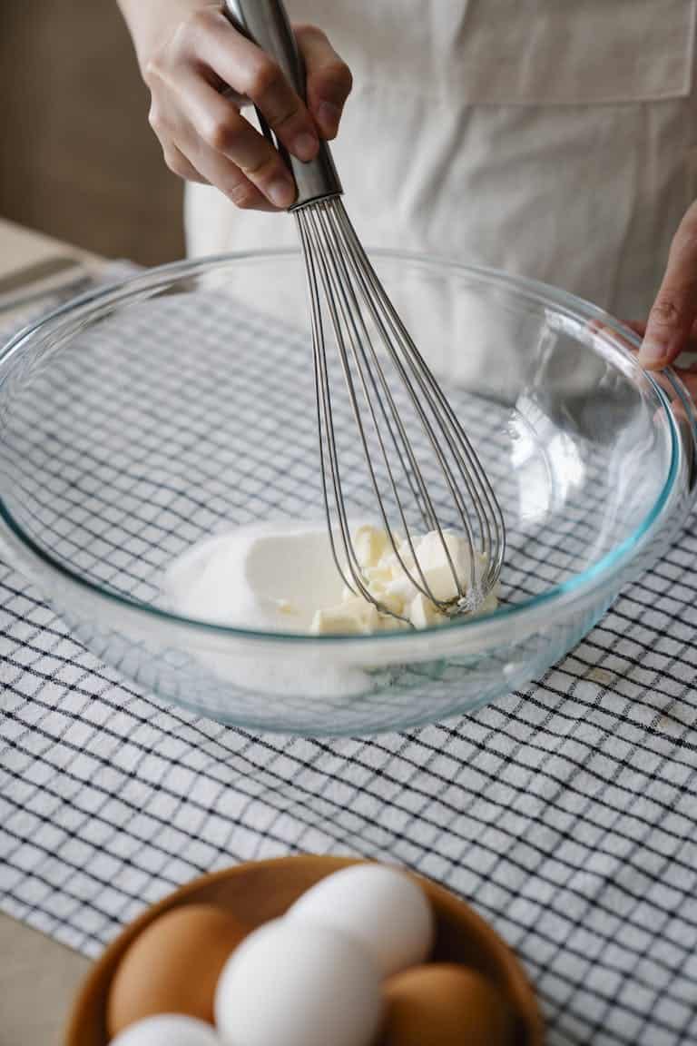 Person mixing ingredients in a glass bowl with a whisk, preparing dough or batter.