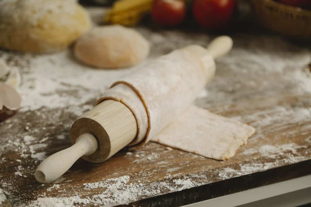 Wooden rolling pin with soft thin dough on table with spilled flour in kitchen