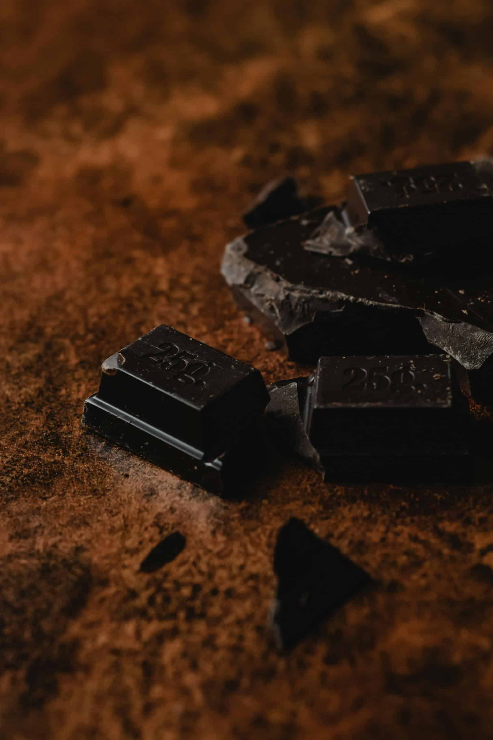 Close-up of dark chocolate pieces on cocoa powder background, showcasing rich texture and color.